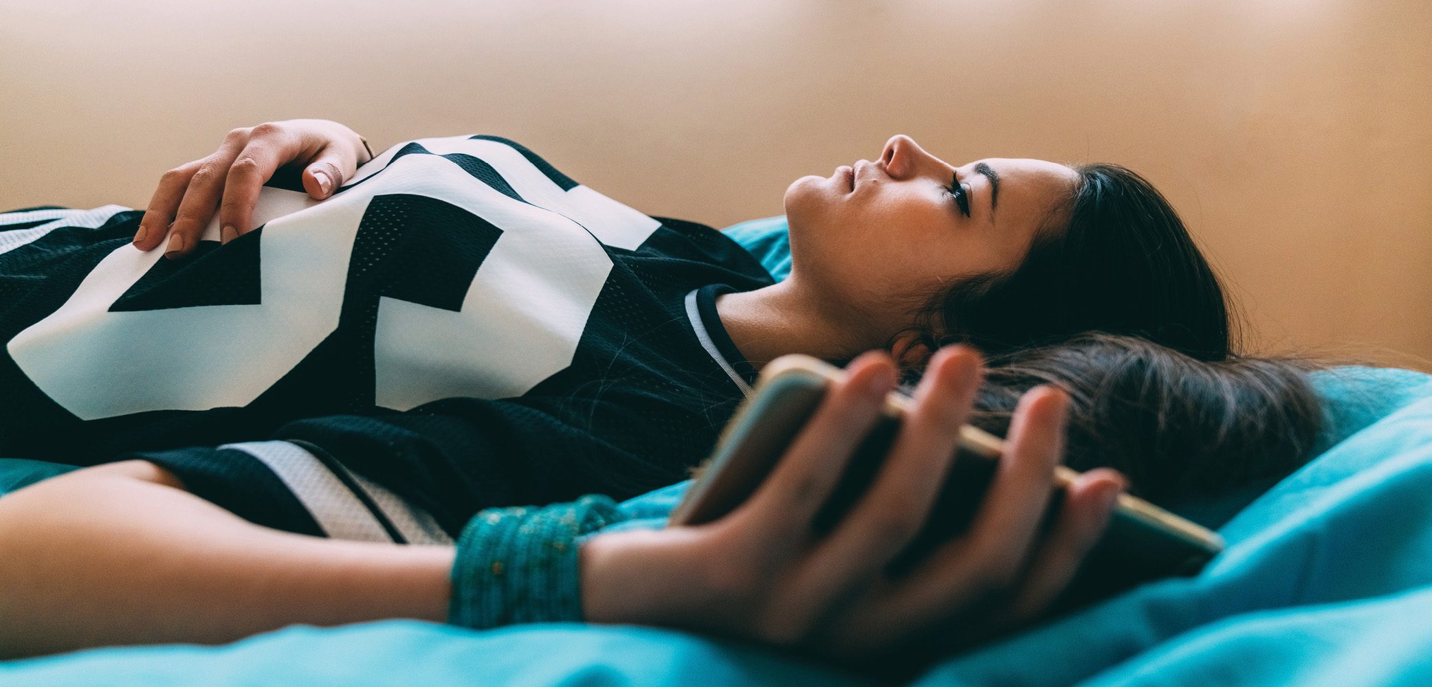 Image of adolescent girl laying in bed with phone in her hand