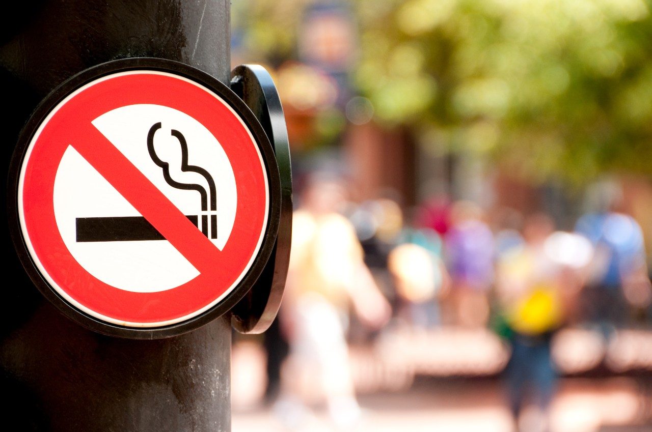 No smoking sign on a post with blurred people in the background
