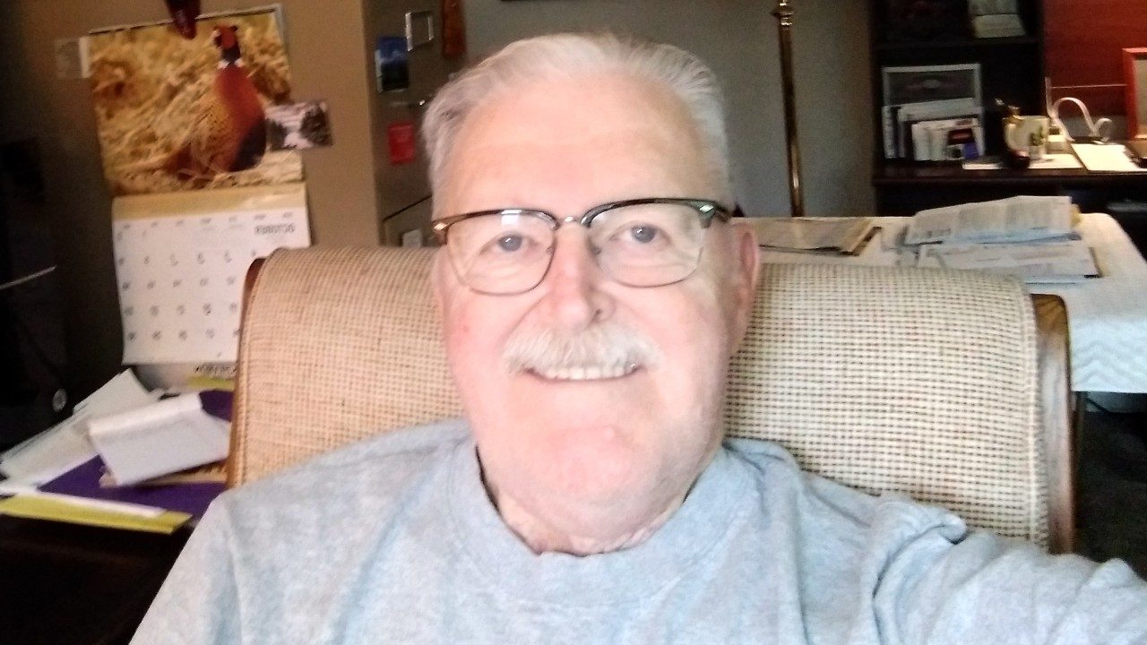 Close-up shot of Robert Clark. He is wearing glasses and a gray shirt, and he is smiling.
