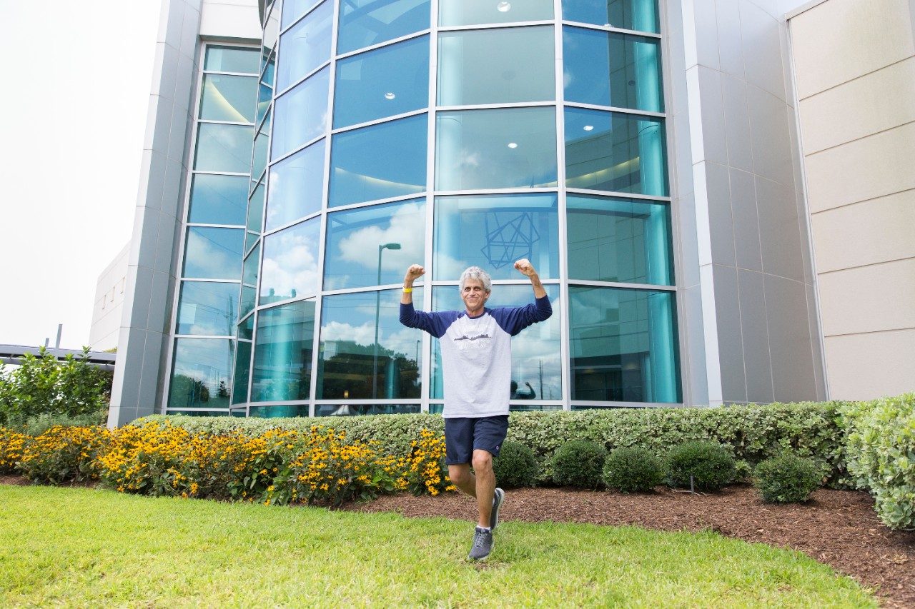 Jerry Iacono poses with his arms in the air outside MD Anderson's Proton Therapy Center