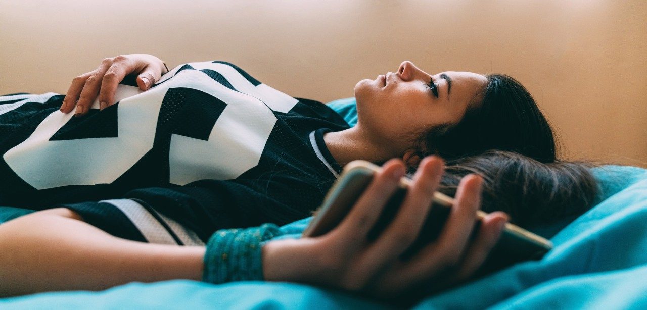 Image of adolescent girl laying in bed with phone in her hand
