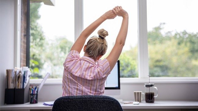 Unidentified woman stretches at her computer desk
