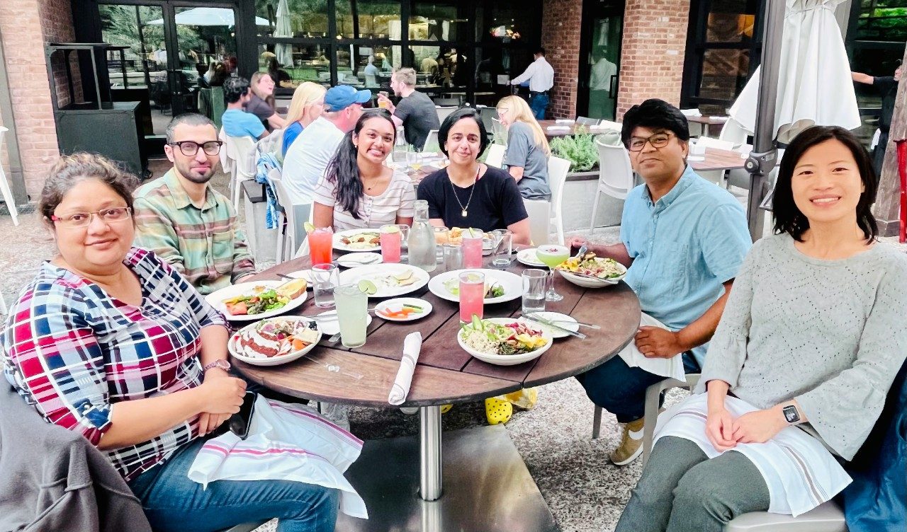 Six people sit around a table of food outdoors